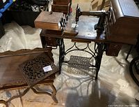 The main antique sewing table with the black Standard sewing machine mounted, featuring the base with treadle and drawers on both sides, with various attachments and the vintage wooden sewing box placed nearby with its lid open.