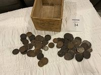 Full view of various old coins spread on white fabric alongside empty small wooden box.
