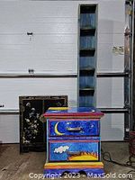 Wide view of three furniture pieces: painted dresser in front, black floral lacquered cabinet behind left, tall narrow softwood shelf behind center/right.