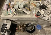 Overview of table with coffee mugs, glasses, cooking utensils, crystal candle holders, non-slip stair treads, and assorted small home decor items