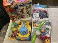Photo showing the sealed box of Super Mario Blow Up Shaky Tower game, blue and yellow bath toy boat, Munchkin Fishin' bath toy with fishing rod, and partially visible Hudson's Bay towel.