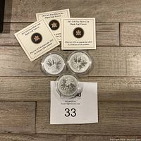Three silver coins in capsules arranged beneath three certificates on wood surface