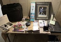 Full lot view on wooden table showing briefcase, framed Leafs player photo, boxed Shotstand, conference speaker, smart watch boxes, headsets, notebooks, and office supplies.