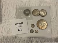 Group view of the lot showing all coins laid out on a white surface, including one sealed coin and smaller worn silver coins.