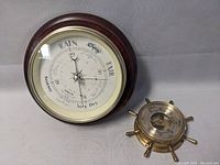 Both barometers displayed, large wooden-framed and smaller ship wheel style on surface