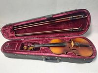 Open hard case containing violin and two bows in fitted burgundy velvet interior