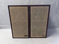 Front view of two rectangular speakers with fabric grills and wood trim, standing side by side.