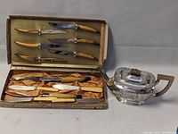 Photo showing assemblage of the tea pot and display boxed cutting utensils with silver plated blades and bone or faux bone handles