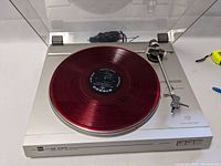 Front view of Dual CS 616Q turntable with red vinyl demonstration disc (not included) on platter, S-shaped tonearm and clear dust cover open