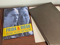 Two hardcover art books, one about Frida Kahlo and Diego Rivera with a colorful dustjacket, the other titled Santa Fe Art with a plain black hardcover and gold lettering on the spine.