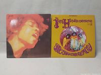 Front covers of two Jimi Hendrix Experience vinyl albums, one a double LP set with close-up face in red hues, the other a single album with yellow psychedelic band photo cover.