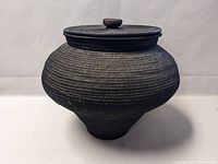 Side view of a large hand woven basket with a fitted lid, showing its rounded shape and dark color.