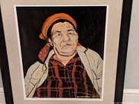 Close-up of lithograph portrait depicting older woman with orange headscarf, red and black plaid shirt, beige jacket, artist signature and date visible on artwork.