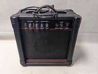 Front view of Meridian AK15G guitar amplifier showing input, overdrive, clean volume, EQ knobs, and power switch with indicator LED, plus front speaker grille.