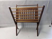 Front view of the mid century wooden magazine stand showing slatted design and vertical cutouts on back panel.