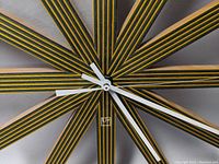 Close up of the clock face showing the yellow and black stripes on the wooden slats and white and black clock hands.