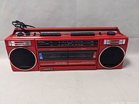 Front view of Sanyo MW703 red cassette radio showing dual speakers, cassette door with lettered sides, and control buttons.