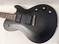 Close-up of guitar body showing dual humbucker pickups, three control knobs, fixed bridge, matte black finish