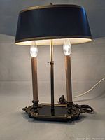 Front view of vintage style table lamp with black oval fabric shade, ornate brass/bronze base, two candle-style bulbs lit