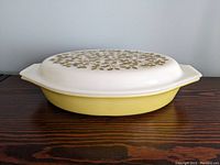 Side view of vintage Pyrex yellow/green 1.5 quart casserole dish with lid on wooden surface.