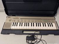 Front view of Yamaha PortaSound P100 electronic keyboard inside black carrying case with power adapter in front.