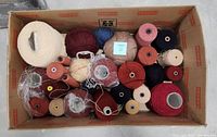 Top-down image of 27 yarn and string rolls in a cardboard box showcasing various colors and sizes including beige, burgundy, red, blue, pink, navy, and white yarn cones and spools.