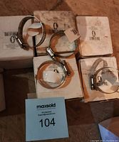 Close up of several individual metal hose clamps laid out on white boxes showing their silver metal band and worm gear tightening mechanism.