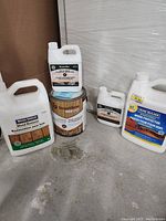 Five wood care product containers including Beautitone End Cut Sealer, Beautitone Wood-Shield Clear Base, Wood-Shield Wood Restorer, and Home Builder Wood Protector, shown on floor.