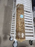Photo of rolled carpet runner on a cart, wrapped in plastic showing light brown color and rolled form