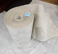 Rolled carpet runner on tiled floor showing intricate light pattern and size indication.