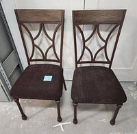 Front view of two identical dining chairs, showing the fabric seat and decorative metal backrest with wooden top rail.