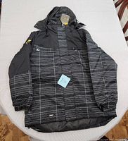 Front view of the black and grey striped winter ski jacket laid flat, showing overall style, hood, and front pockets.