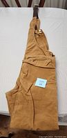 Folded tan-colored heavy-duty Carhartt coveralls with adjustable straps on a white background showing front side with pockets.