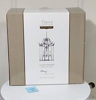 Photo of the boxed Patriot Lighting Macy Collection 3-light pendant chandelier with branding and dimensions visible on the packaging.