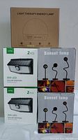Full lot image showing 3 boxes of 2-pack 300 LED Solar Motion Sensor Lights, 2 Sunset Lamp boxes, and 1 Light Therapy Energy Lamp box in original packaging.