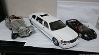 Photo of three model cars from a side and top angle including the silver Jaguar SS, white Lincoln limousine, and black Ferrari F50 models with visible detailed interiors and exterior features.