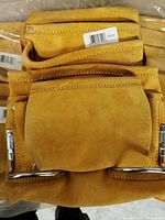 Close-up image of stacked leather tool holder belts showing large front pockets, metal hammer loops, and stitched edges.