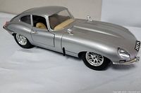 Side and front angle showing silver metallic finish, detail on hood vents, chrome side mirrors, and wheels; clear windows with visible interior.