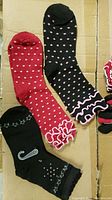 Photo showing three girls' socks designs laid flat: black with pink polka dots and pink ruffles, red with white polka dots and pink ruffles, black with silver stars and pin graphic.