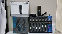 All four items arranged: boxed AKG P120, Logitech G935 box, mixer unit and Budbof microphone