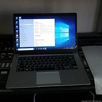 Laptop powered on showing Windows 10 Home desktop and open system properties on-screen.