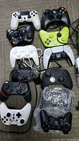 Top down view of various wired and wireless Xbox and PlayStation controllers in black, white, and neon green laid on a carpet.