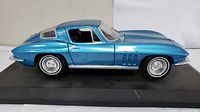 Side profile of blue Maisto 1965 Chevrolet Corvette diecast model car on display base.