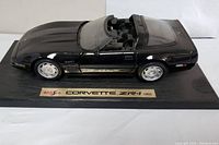 Full side view of black model car on base showing sleek body lines and convertible roof panel, emphasizing model quality.
