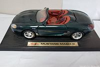 Green Maisto Mustang Mach 3 convertible model car on black display base with gold nameplate.