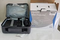 Elephas W13-M mini projector inside a grey soft carrying case next to the original packaging box. The case is open, and the projector is visible inside.