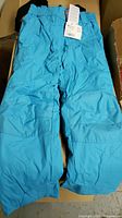 Full view of bright blue kids snow pants with suspenders, showing front, legs, elastic waistband, and reinforced knee area.