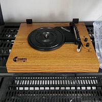Wood-finished turntable with black platter and tonearm, placed on a black shelf.