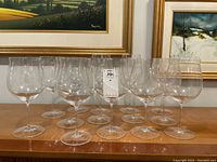 Front view showing all 14 glasses in two rows on wooden table under framed artwork