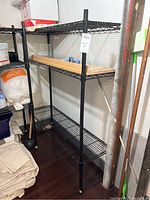 Full view of black metal wire shelving unit showing three shelves and tubular legs with plastic feet.